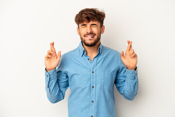 Young mixed race man isolated on grey background crossing fingers for having luck