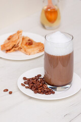 Glass coffee with foam milk with honey on white wooden table.