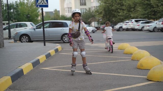 Little girl learns to roller skate. Kid is dressed in protection and a helmet, a schoolgirl rides along the road on roller skates. Children is transport, sports games, happy childhood