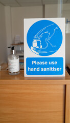 Norwich, Norfolk, UK – November 05 2021. Sign advising visitors to sanitise their hands, and a bottle of hand sanitiser, during the Covid pandemic in a commercial office