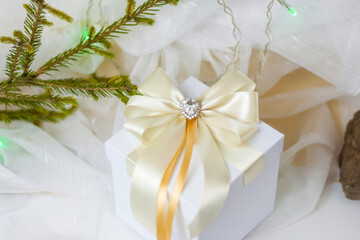 A Christmas gift decorated with a beautiful bow on a light background with a twig, if. Selective focus. the concept of Christmas and New Year.