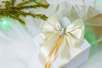 A Christmas gift decorated with a beautiful bow on a light background with a twig, if. Selective focus. the concept of Christmas and New Year.