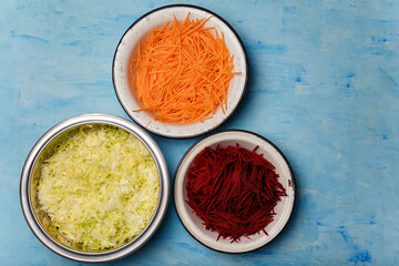 Three bowls of beetroot, carrots and cabbage cut into thin strips on blue painted wooden background. Vegetarian, organic, healthy food, diet, nutrition. Top view, copy space.