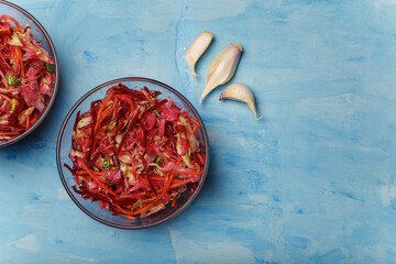 Two bowls of salad called Brush. Beetroot, carrots and cabbage cut into thin strips with garlic on blue wooden background. Vegetarian, organic, healthy food, diet, nutrition. Top view, copy space.