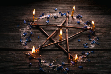 Branch Pentagram - witchcraft tools of natural wood. Wooden pentagram with candles, small stones and petals of delphinium. Occultism and mysticism