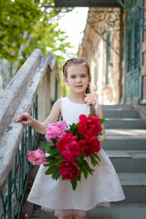 Beautiful little girl in white dress with big peonies bouquet. Spring blossom and carefree childhood concept.