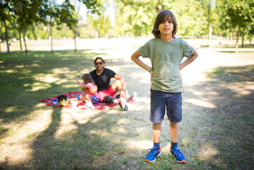Portrait of cute little boy on picnic in park. Dark-haired boy in shorts and green t-shirt posing,...