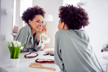 Portrait of attractive cheerful girl looking at mirror applying daily cream at light white home...