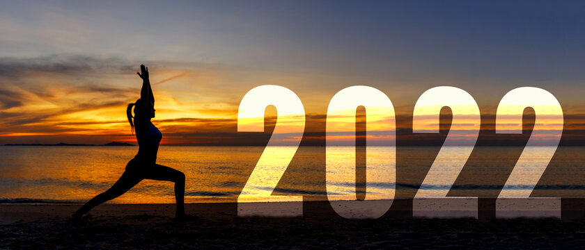 Happy new year card 2022. Silhouette lifestyle woman yoga practicing yoga standing as part of Number 2022 near the beach at sunset. Healthy and Holiday Concept