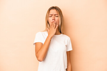 Young caucasian woman isolated on beige background yawning showing a tired gesture covering mouth...