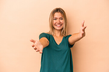 Young caucasian woman isolated on beige background showing a welcome expression.