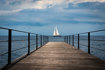 Small empty wooden pier and a sailing boat in the horizon of the Mediterranean sea, Italy, Europe.