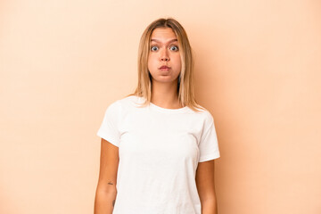 Young caucasian woman isolated on beige background blows cheeks, has tired expression. Facial expression concept.