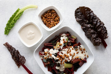 Rainbow chard salad with tahini sauce and pine nuts in bowl. Vegan meal Swiss chard leaves. Top view.