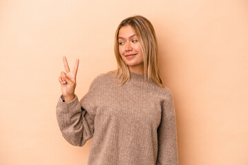 Young caucasian woman isolated on beige background joyful and carefree showing a peace symbol with fingers.