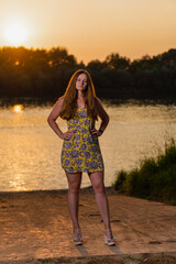 Girl in a short yellow dress on the river bank, summer sunset.