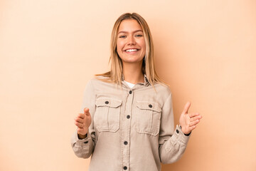 Young caucasian woman isolated on beige background holding something with both hands, product presentation.