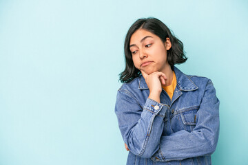 Young latin woman isolated on blue background looking sideways with doubtful and skeptical expression.