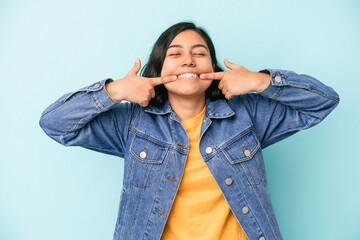 Young latin woman isolated on blue background smiles, pointing fingers at mouth.