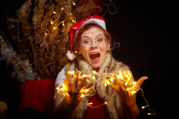 A cheerful dwarf with garlands in his home. Assistant of Santa Claus in a red hat and with glowing...