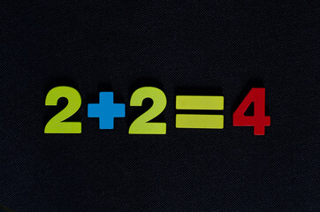 Simple mathematical equation made from colorful wooden numbers on black background