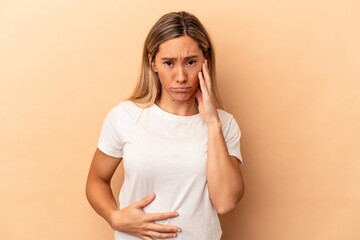 Young caucasian woman isolated on beige background blows cheeks, has tired expression. Facial...