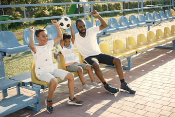 Black father and two his multiracional sons watching football game on stadium