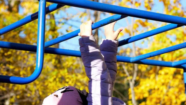 A teenage girl walks with her hands on a horizontal staircase in autumn. Children's sports, training of arm muscles.