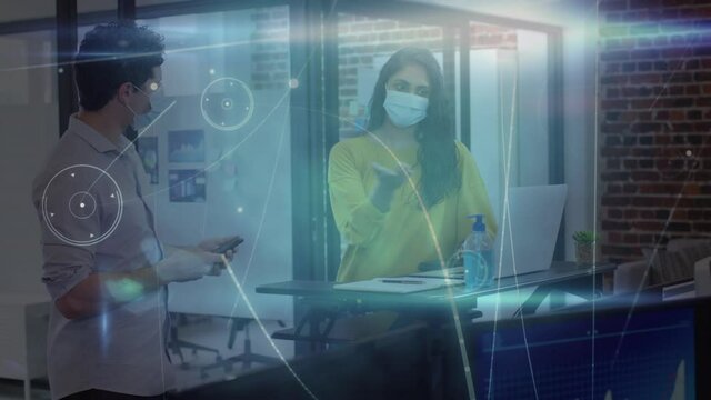 Animation of network over male and female creative colleagues in face masks working in office