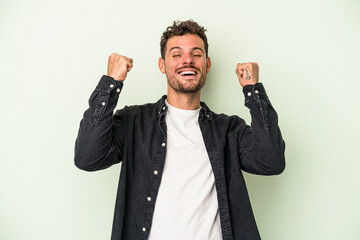 Naklejka premium Young caucasian man isolated on green background celebrating a victory, passion and enthusiasm, happy expression.