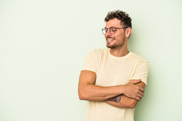Young caucasian man isolated on green background smiling confident with crossed arms.