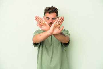 Young caucasian man isolated on green background doing a denial gesture