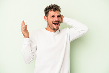 Young caucasian man isolated on green background screaming with rage.