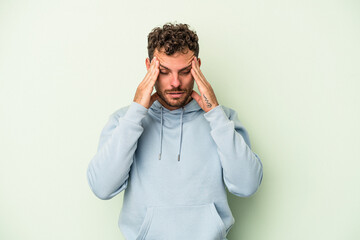 Young caucasian man isolated on green background having a head ache, touching front of the face.