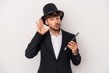Young arab wizard man holding a wand isolated on white background trying to listening a gossip.