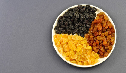 Raisins are light, black, brown on a white round plate. On a gray background. Close-up. Copy space.