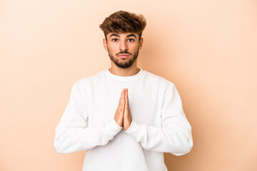 Young arab man isolated on beige background praying, showing devotion, religious person looking for...