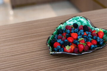 Designer plate with fresh raspberries, blackberries, blueberries, strawberries on a bed. Healthy breakfast. Soft selective focus, artistic noise.
