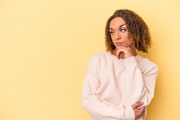 Young latin transsexual woman isolated on yellow background looking sideways with doubtful and skeptical expression.