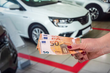 hands of a young woman holding a euro banknote on a background of cars