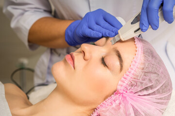 Fototapeta na wymiar Young caucasian woman having ultrasonic peeling with ultrasound device in a cosmetic beauty salon