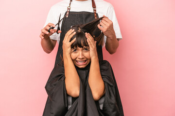Young mixed race woman getting a haircut at the hairdresser isolated on pink background