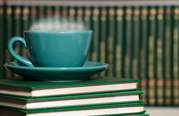 table with green cup of hot coffee, with books.
