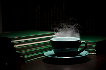 table with green cup of hot coffee, with books, black background, space for text.