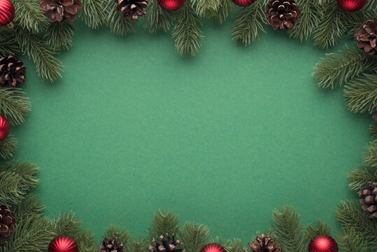 Top view photo of pine branches with cones and red christmas tree balls on isolated green background with blank space in the middle