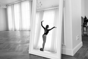Fototapeta na wymiar girl gymnast, is engaged with gymnastic objects in a light room, she is in a black leotard, performs exercises.