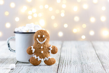 Fototapeta na wymiar A white cup of winter hot drink with marshmallows and gingerbread man on a white wooden background with bokeh.