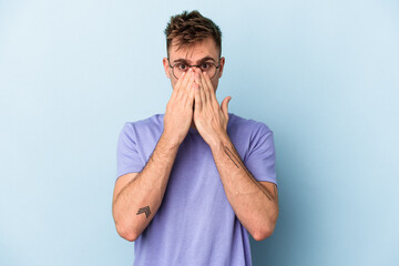 Young caucasian man isolated on blue background shocked, covering mouth with hands, anxious to discover something new.