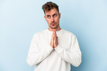 Young caucasian man isolated on blue background praying, showing devotion, religious person looking...