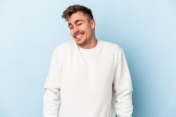 Fototapeta premium Young caucasian man isolated on blue background laughs and closes eyes, feels relaxed and happy.